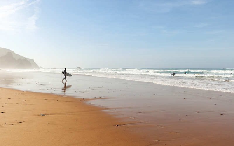 Wit strand met surfers en een helderblauwe lucht