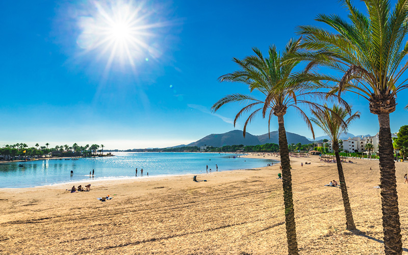 Strand met palmbomen, zon, blauw water en bergen in de verte