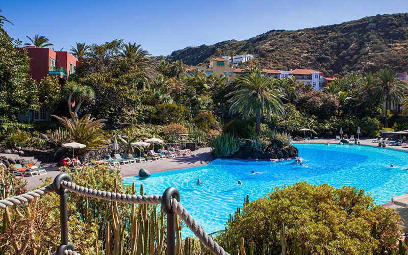 zwembad omgeven door groene tuin met palmbomen en ligbedjes