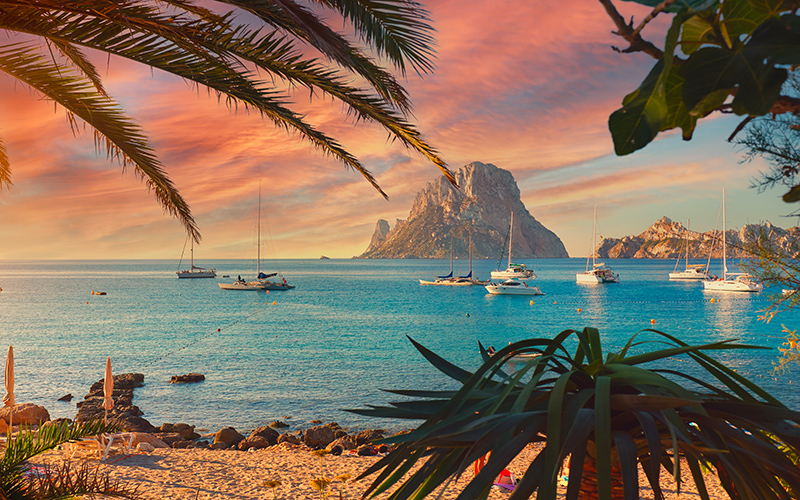 Uitkijkpunt op de Balearen waarbij je palmbomen, een blauwe zee met bootjes en een rots ziet