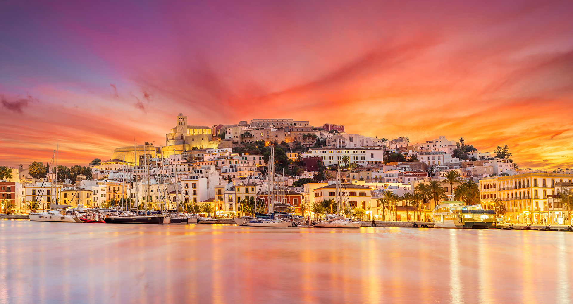 Uitzicht vanaf het water op de winkels in Ibiza, met een schitterende rood/roze lucht