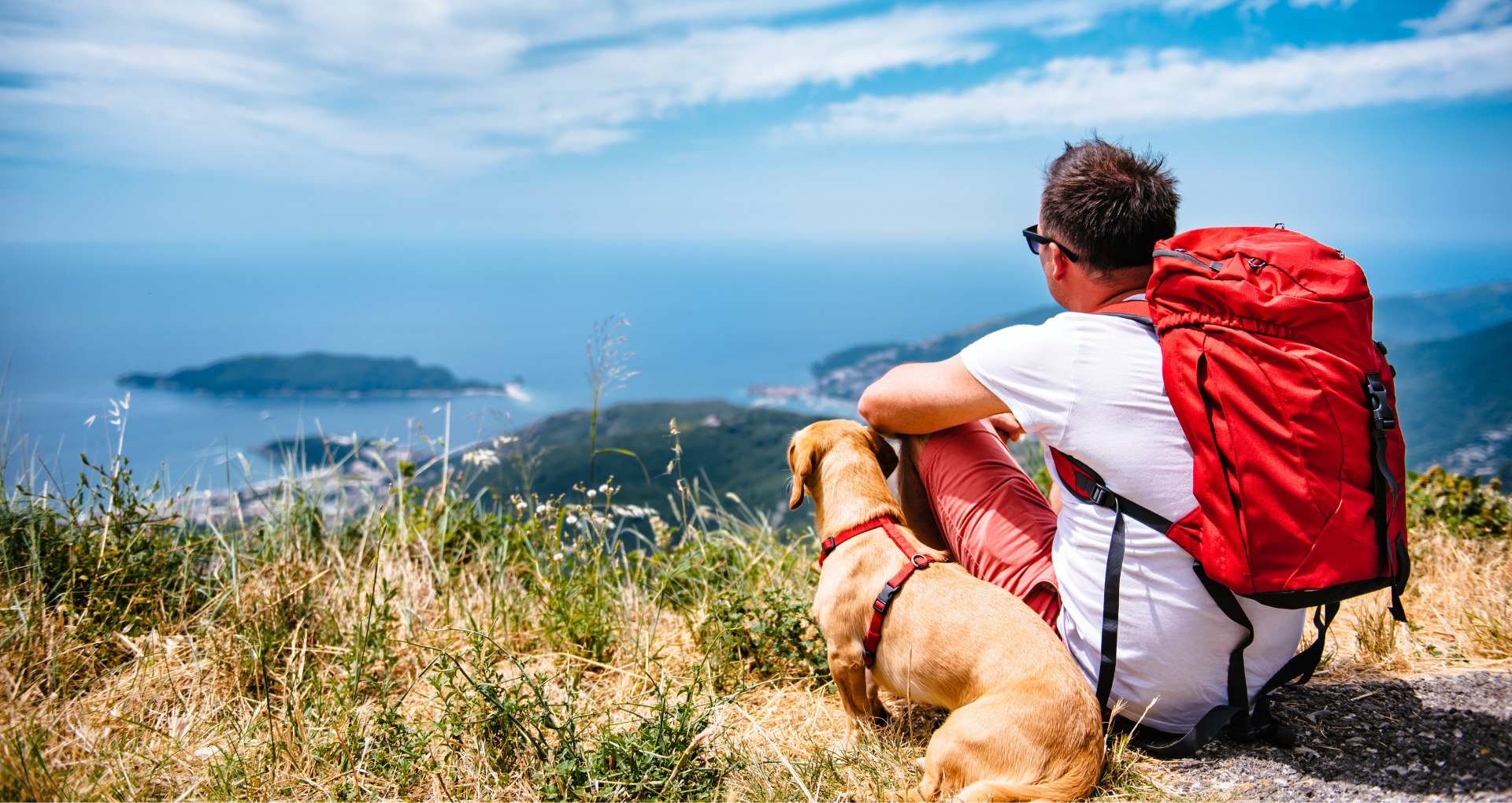 Man met hond en rugzak uitkijkend over zee vanaf berg