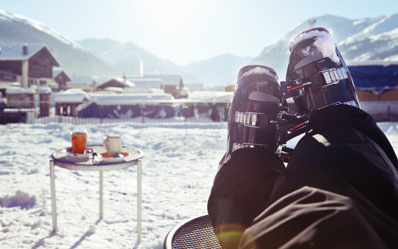 uitzicht op benen met skischoenen van persoon die uitkijkt over besneeuwde bergtoppen