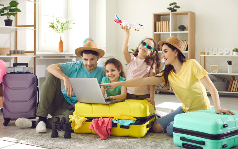 gezin met twee kinderen zitten met koffer op de grond achter laptop vakantie te boeken