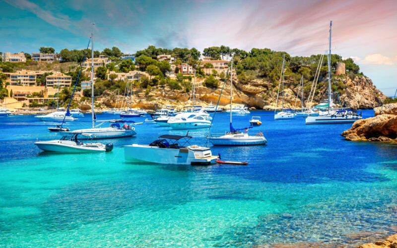 rotskust van Mallorca met op voorgrond witte bootjes in een helderblauwe zee