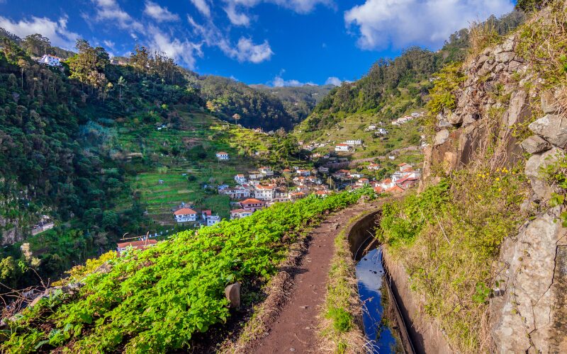 Uitzicht vanaf wandelpad op een vallei met groene bergen op de achtergrond en een dorpje met witte huisjes, op Madeira