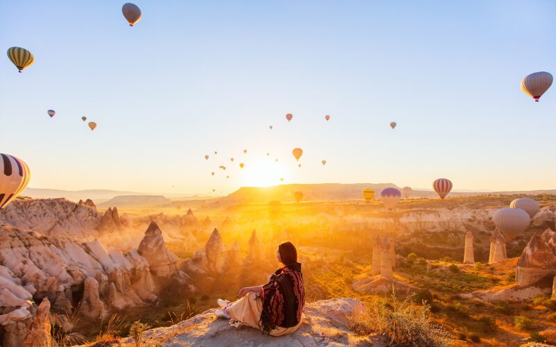 Vrouw kijkt uit over luchtbalonnen tijdens zonsondergang Cappadocië, Turkije